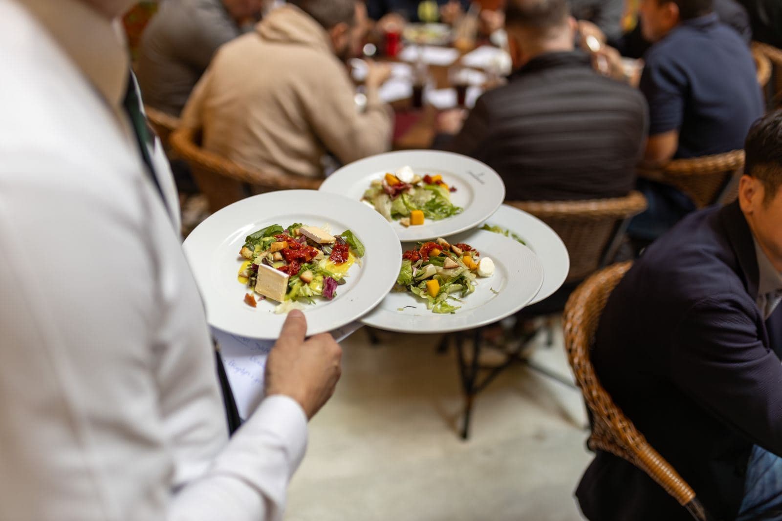 A waiter carrying plated salads through a dining room.